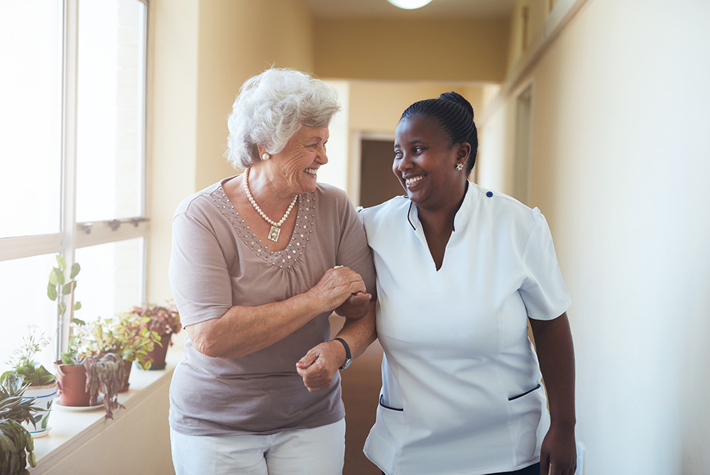 Carer with senior woman walking through care facility
